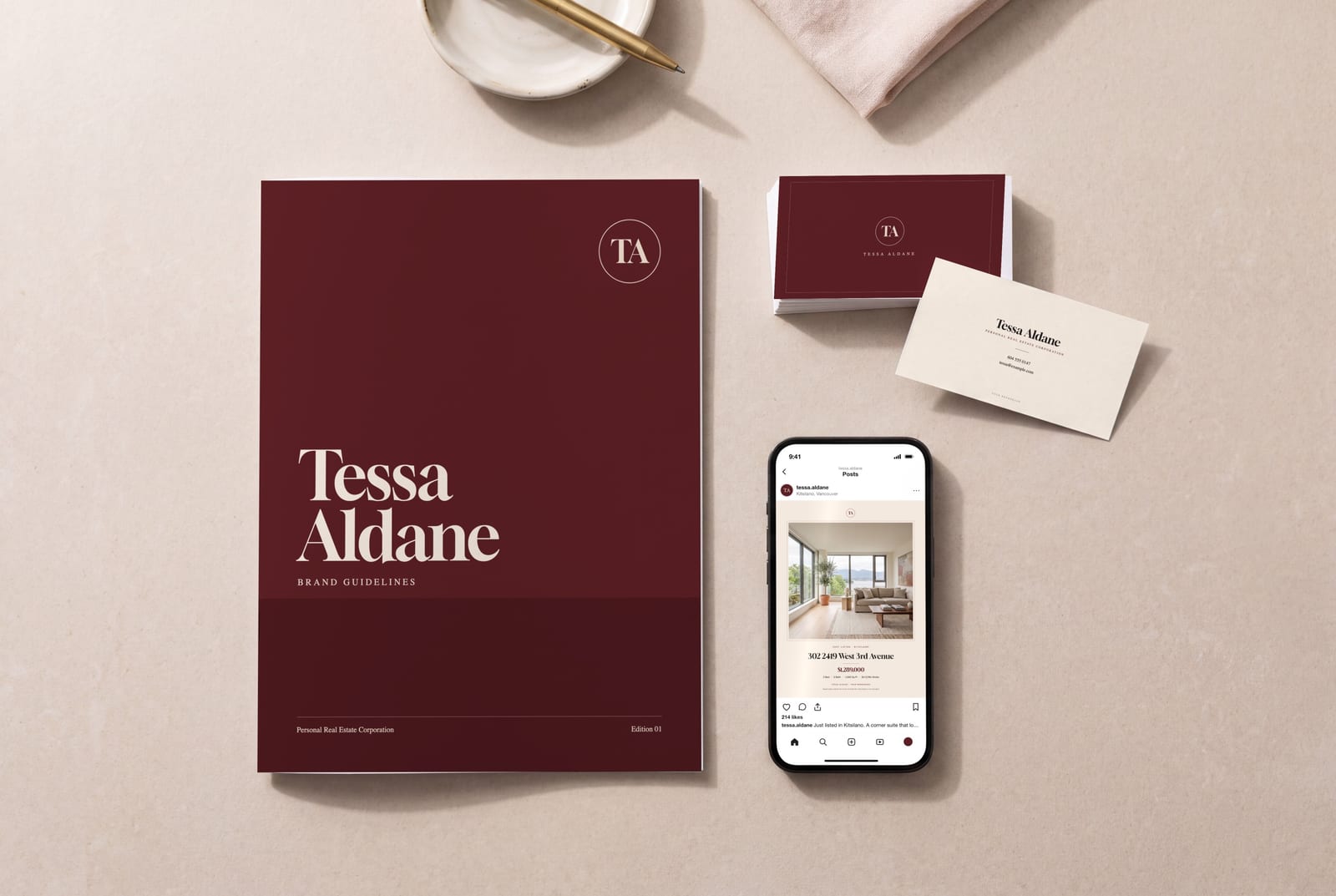 A sample agent's brand kit on a table: the oxblood guidelines booklet, a stack of business cards and a phone showing a listing post