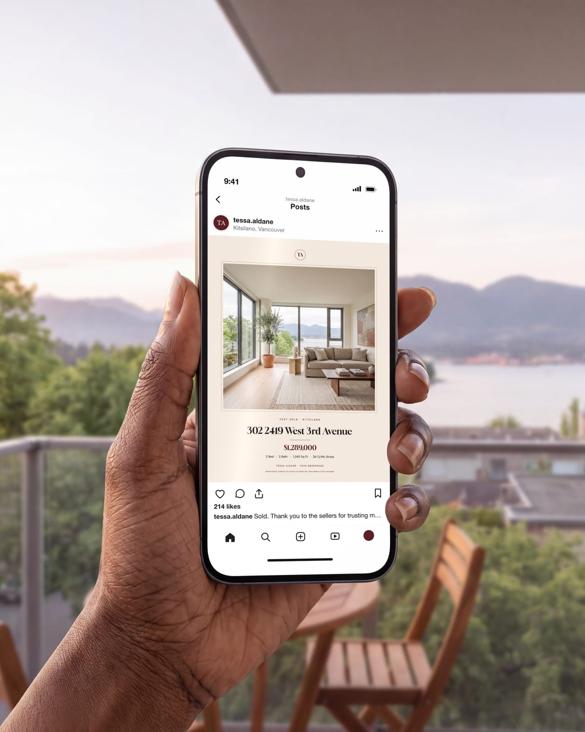 A hand holding a phone with a sample agent's Just Sold post, on a balcony